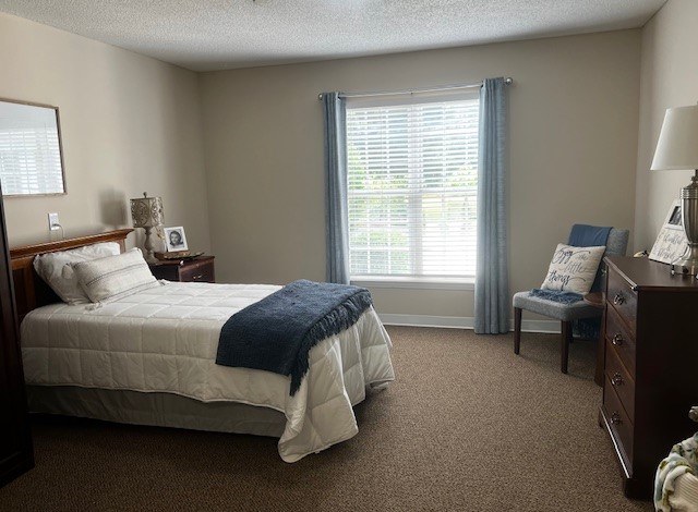 A bedroom with a bed, chair, and window at Spring Arbor of Rocky Mount